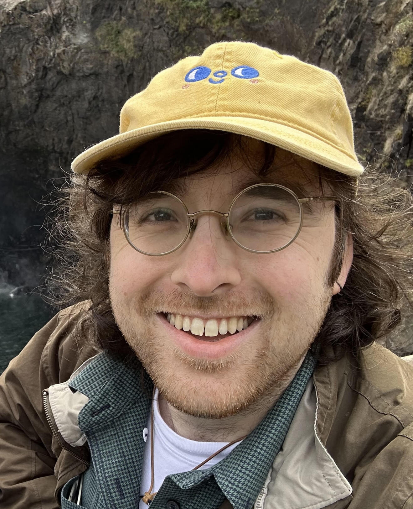 Stu Alexander Headshot of man with glasses and yellow hat standing in front of rocks
